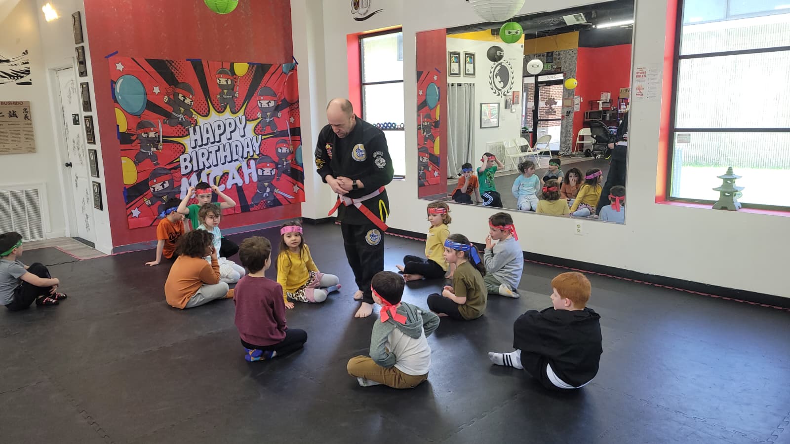 Instructor standing in a circle of seated children leading a birthday party activity in the Burning Tree MMA gym