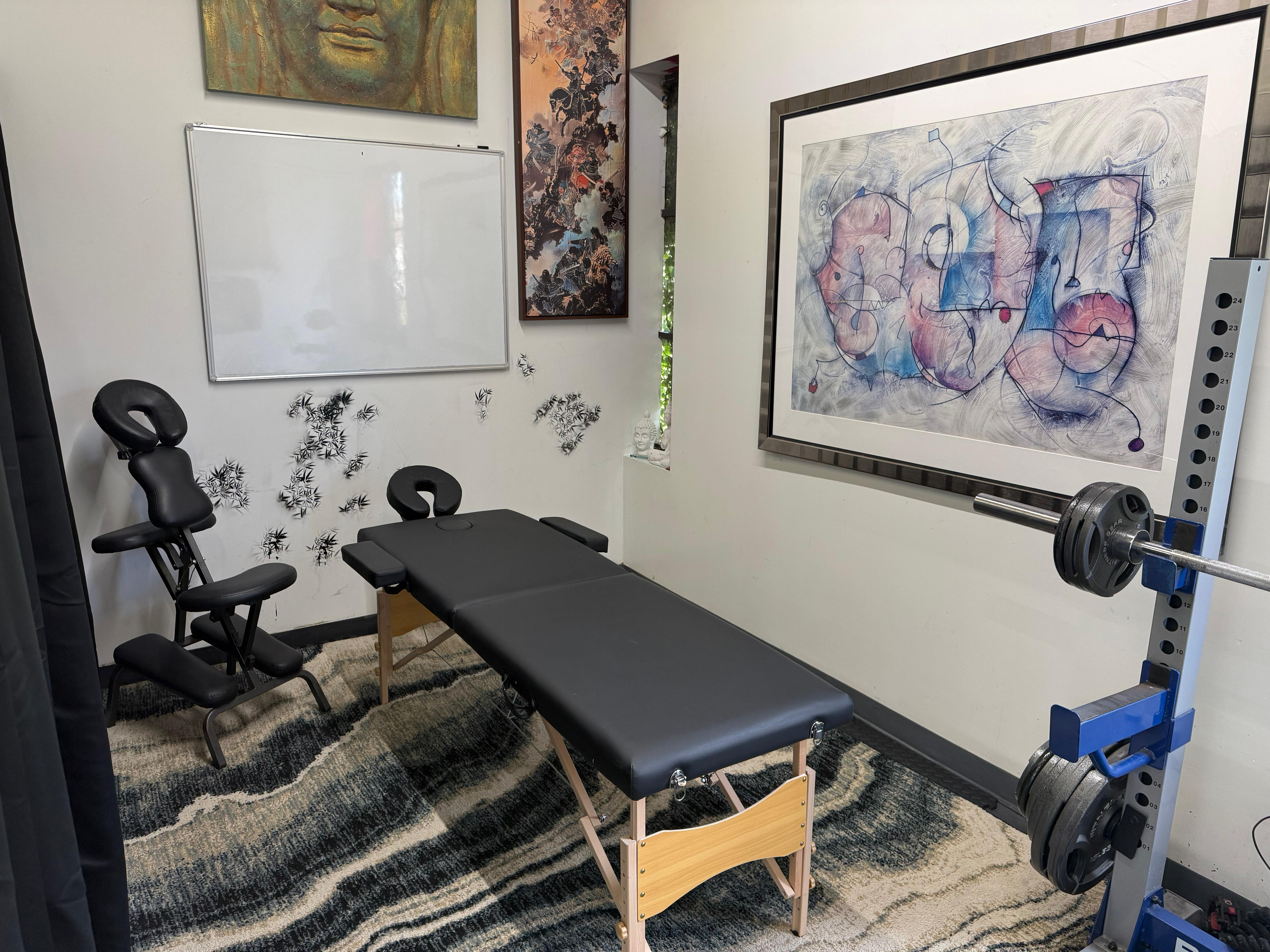 Wellness room interior with a massage table, massage chair, whiteboard, and artwork on the walls
